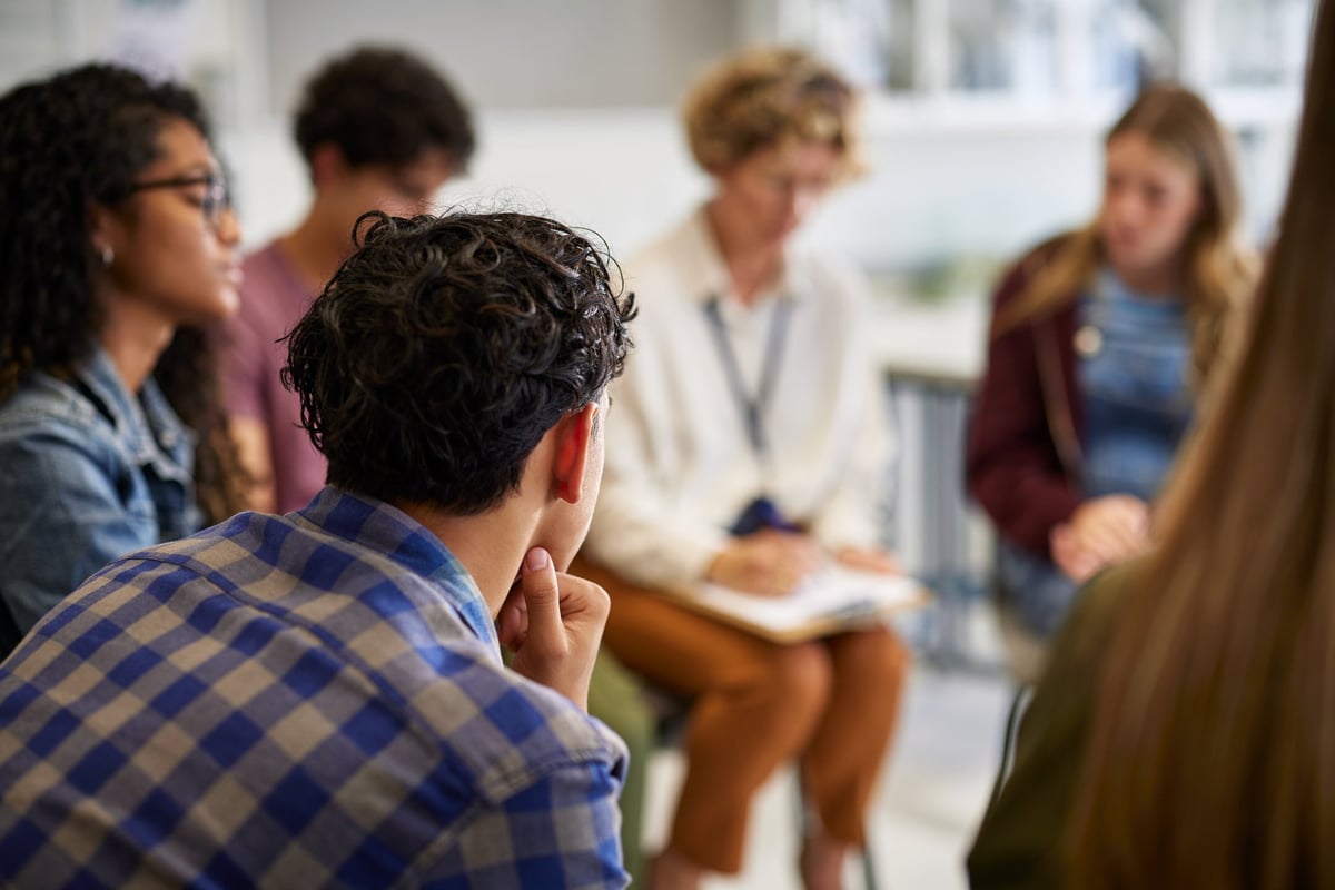 Teenagers sitting in a circle with counselor during a group discussion on emotional well-being