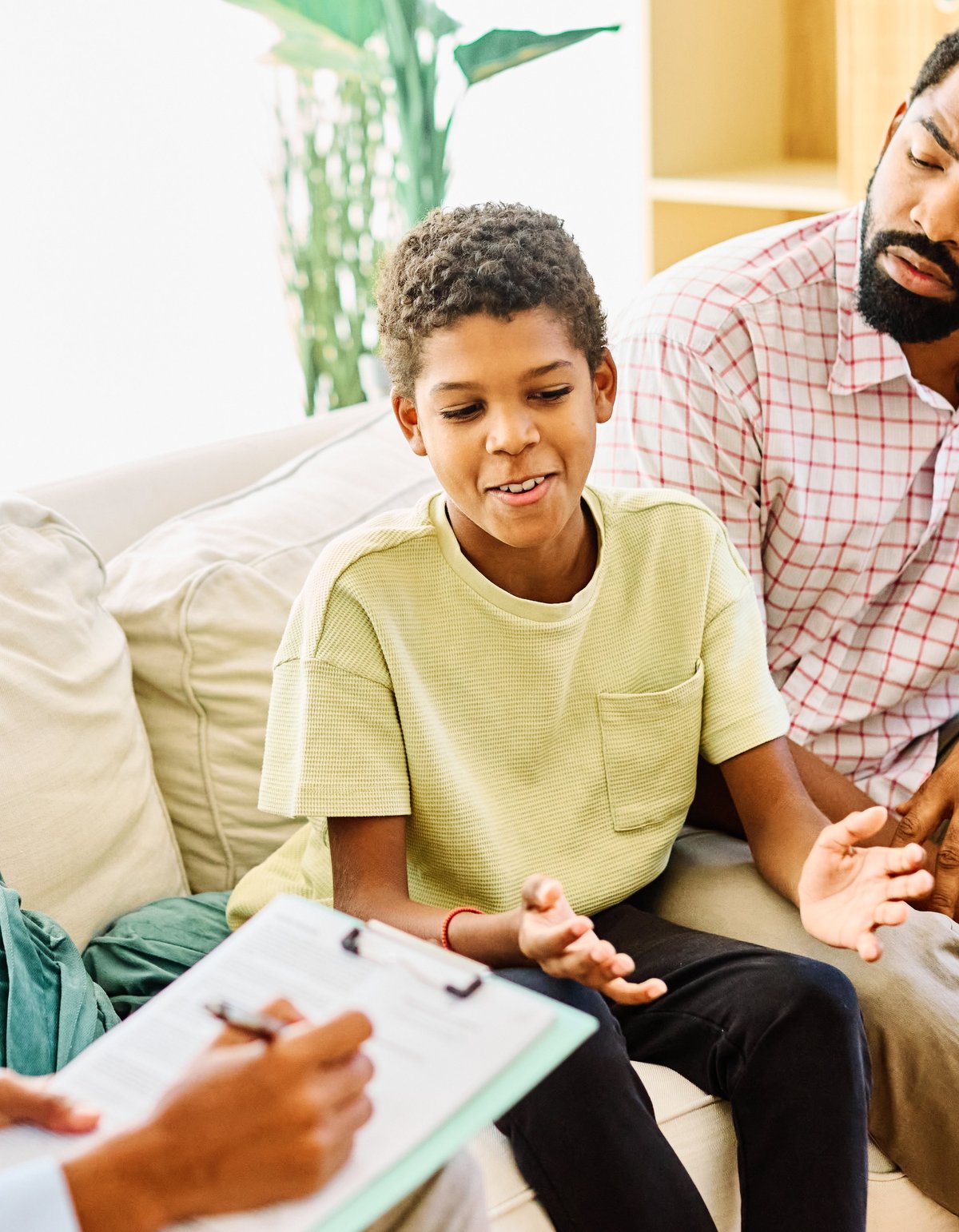 Father with his teenage son boy at meeting with social worker, psychologist discussing mental health family sitting on sofa in psychotherapist office