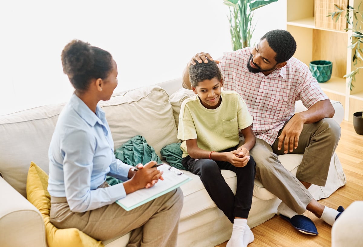 Father with his teenage son boy at meeting with social worker, psychologist discussing mental health family sitting on sofa in psychotherapist office